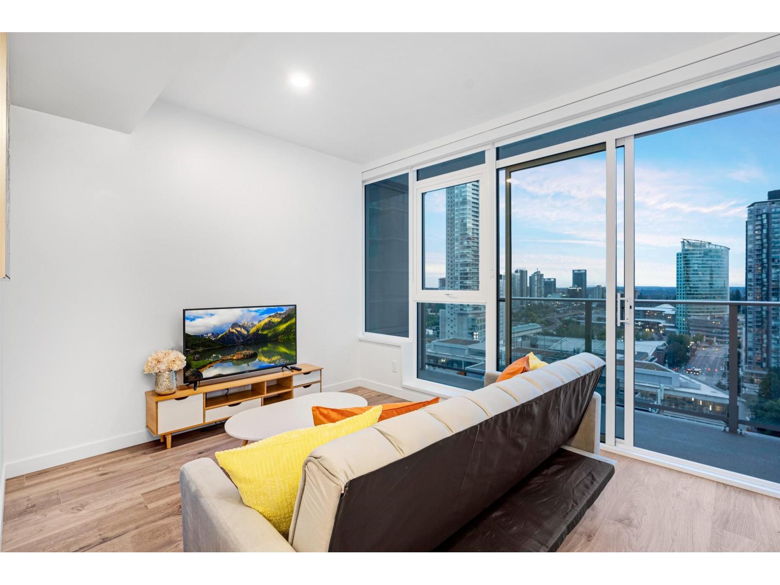 A living room with a couch, a television, and a window overlooking a cityscape.