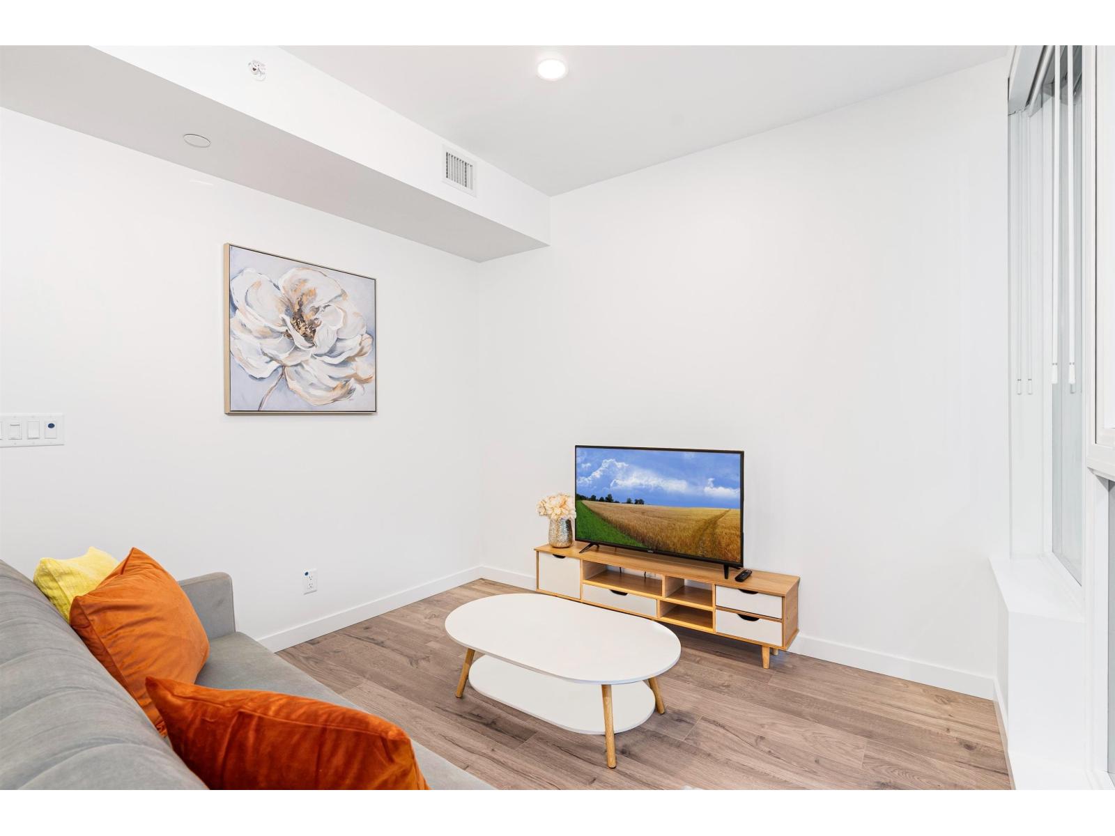 A living room with a grey couch, a white coffee table, and a television on a wooden stand.