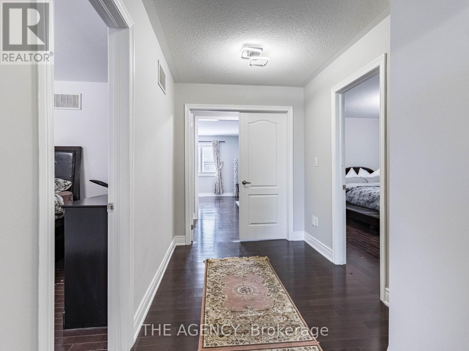 A hallway with a rug on the floor and a bedroom visible through the door.