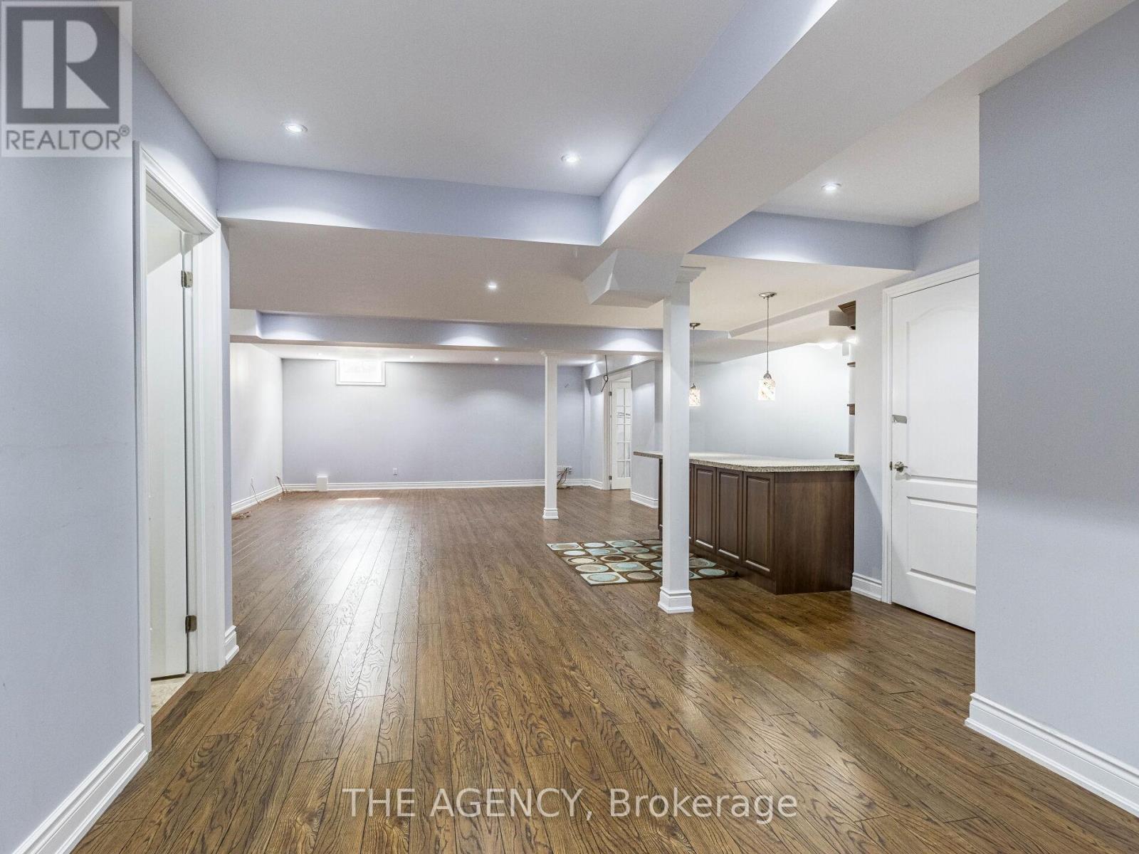 A spacious room with wooden floors and white walls, with a logo that reads "REALTOR" in the top left corner.