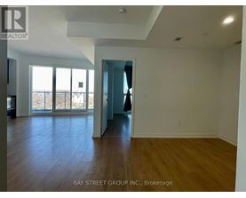 A spacious room with wooden flooring and a view of the outdoors through large windows.