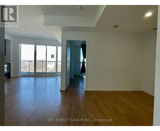 A spacious room with wooden flooring and a view of the outdoors through large windows.