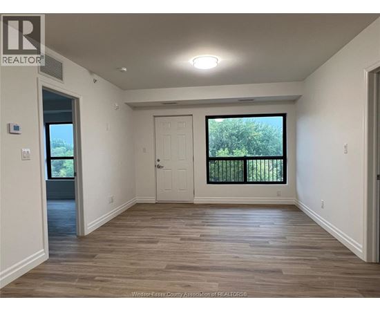 A spacious room with wooden flooring and a large window with a view of trees.
