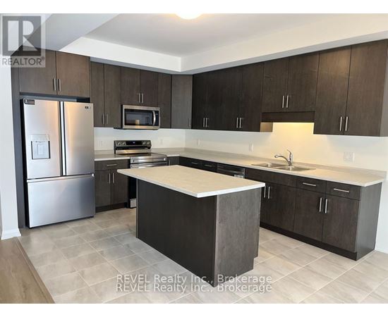 A kitchen with a refrigerator, microwave, oven, sink, and cabinets.