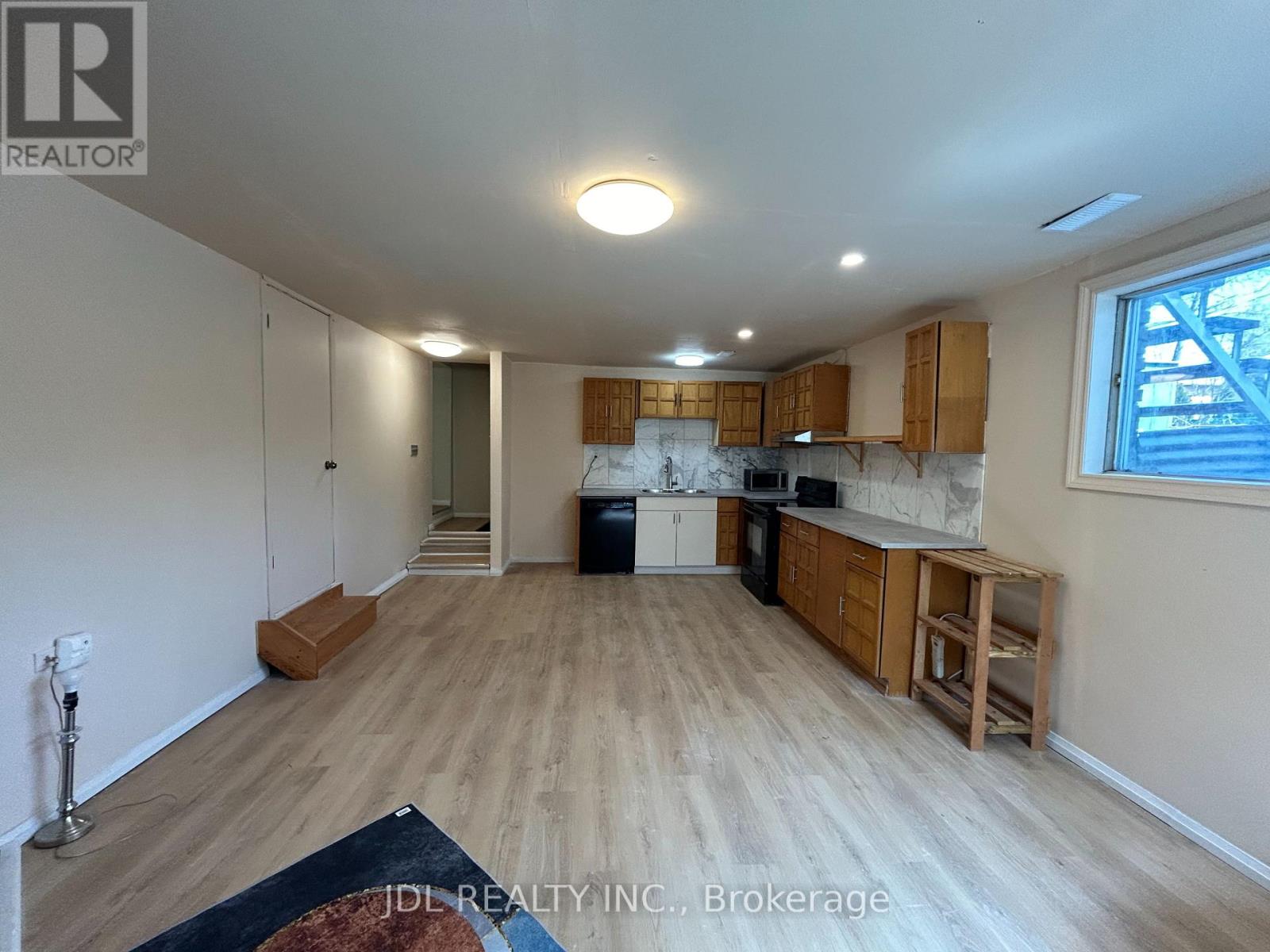 A spacious living room with wooden flooring and a kitchen area in the background.