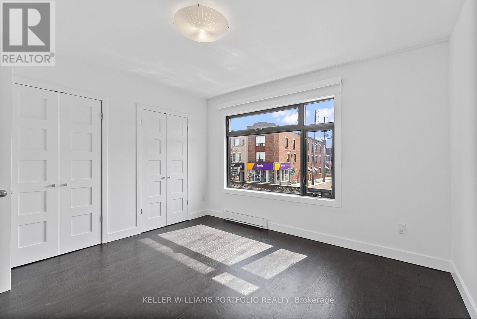 A real estate listing photo of a white bedroom with a large window and a view of the city.