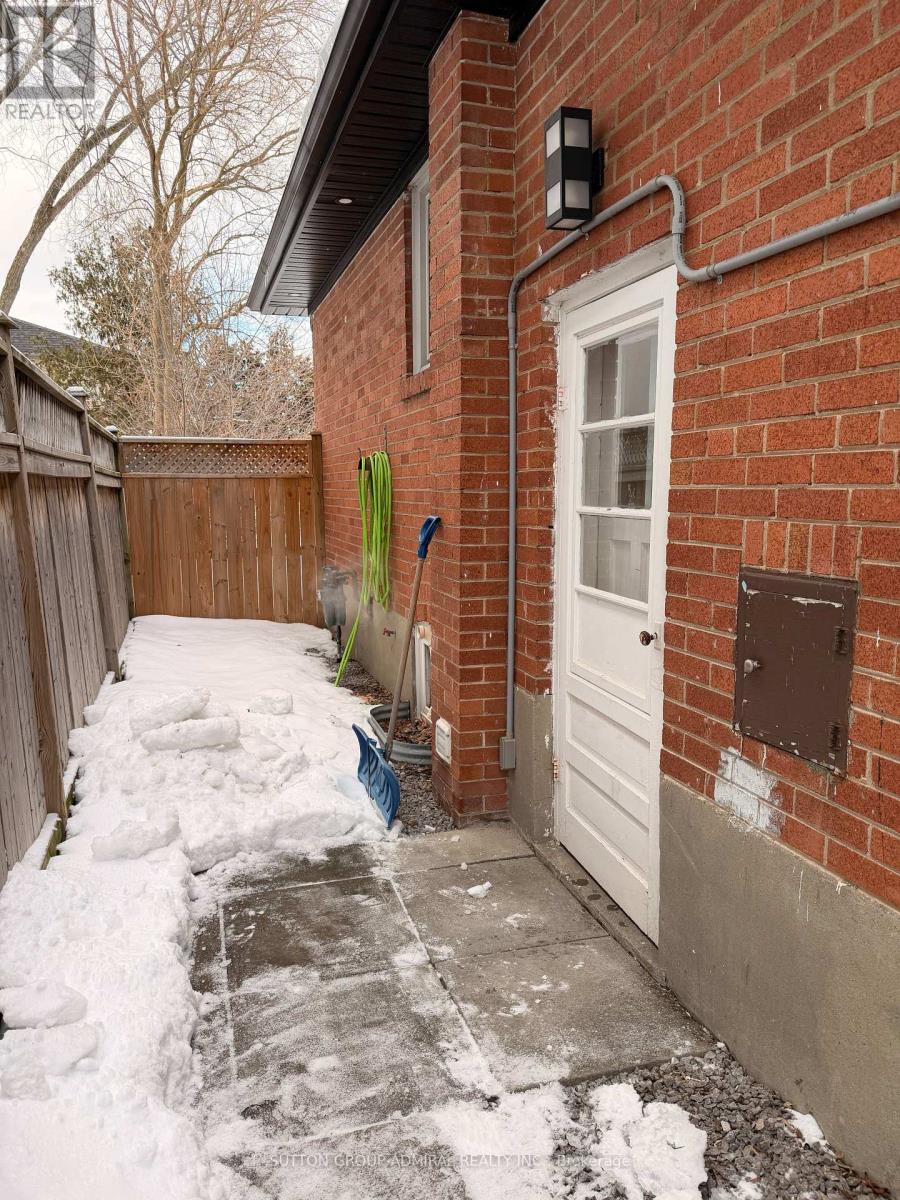 A snow-covered walkway leads to a white door on a red brick house.