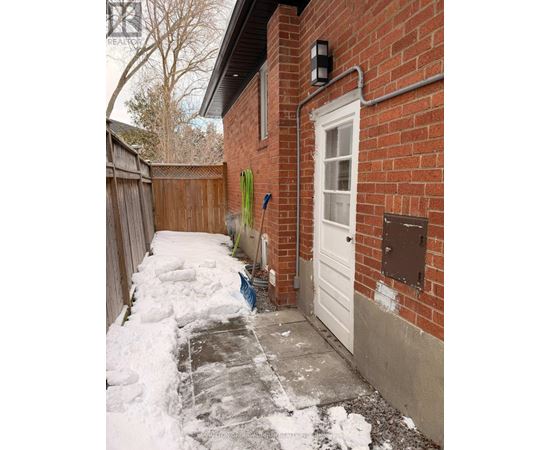 A snow-covered walkway leads to a white door on a red brick house.