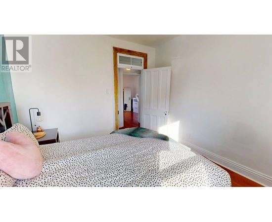 A bedroom with a bed, nightstand, and a doorway leading to another room.