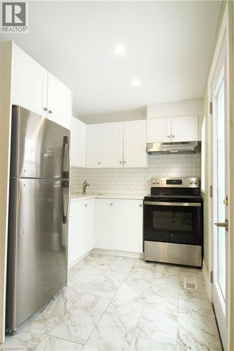 A kitchen with a refrigerator, oven, and stove.