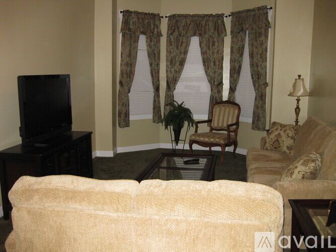 A living room with a television, chair, and window with curtains.