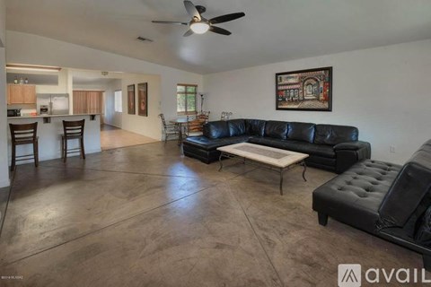 A living room with a black leather couch and a fan on the ceiling.
