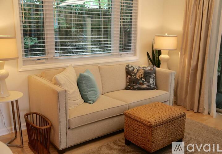 A living room with a beige couch, a wicker ottoman, and two lamps.