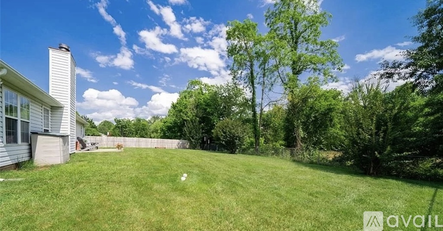 A backyard with a white house, green grass, and trees.