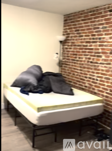 A bed with a white mattress and grey pillows is in front of a brick wall.