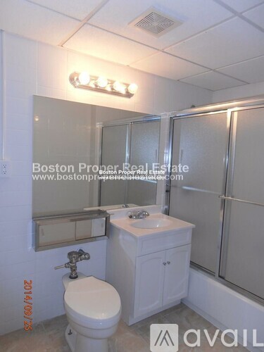 A white bathroom with a toilet, sink, mirror and shower.