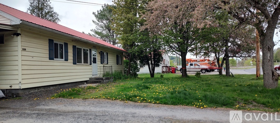 A yellow house with a red roof is surrounded by trees and a dirt path.