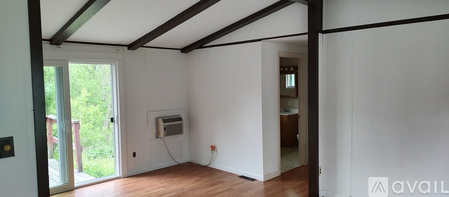 A room with white walls and wooden floors, with a doorway leading to another room.