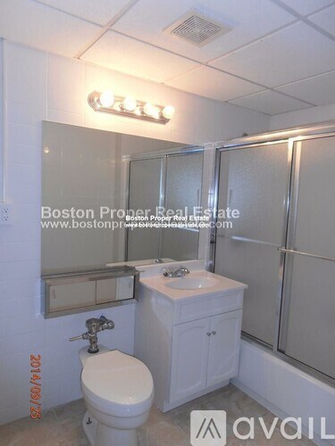 A white bathroom with a toilet, sink, mirror and shower.