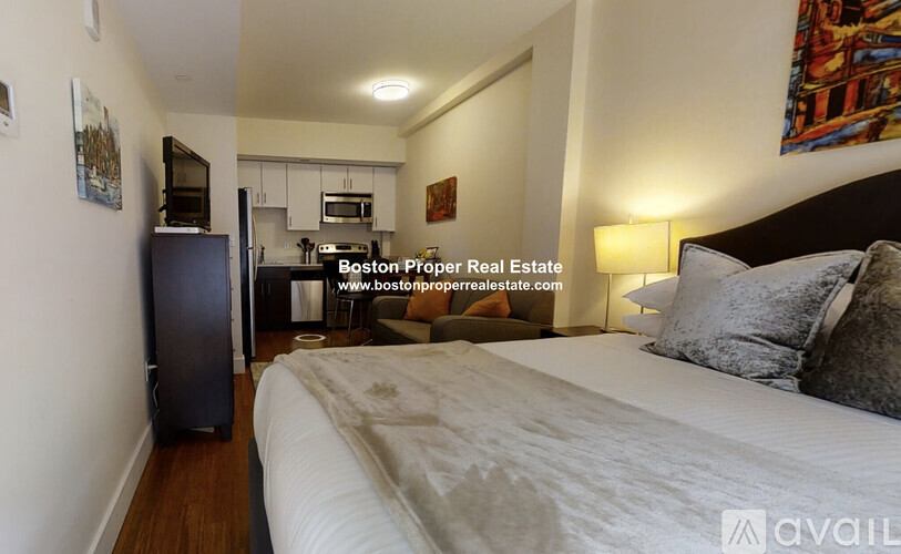A bedroom with a bed, a refrigerator, and a painting on the wall.