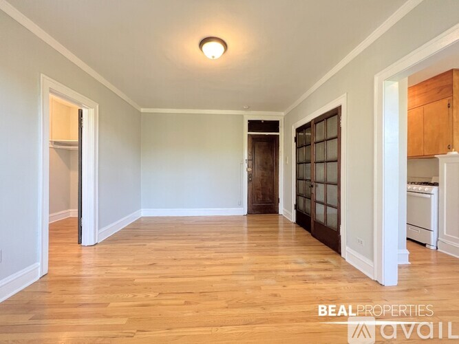 A spacious room with wooden floors and white walls, with a kitchen area visible in the background.
