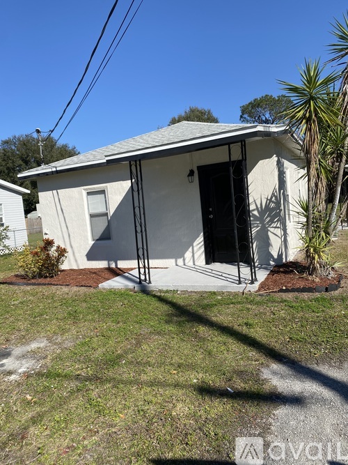 A small white house with a black door and a window is surrounded by a grassy area.