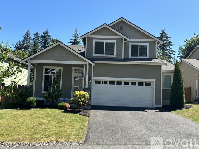 A two-story house with a garage is surrounded by a well-kept lawn and trees.