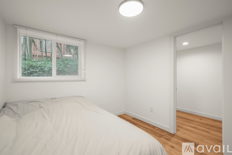 A bedroom with a bed, a window with blinds, and a wooden floor.