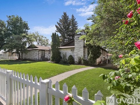 A white picket fence surrounds a house with a stone chimney.