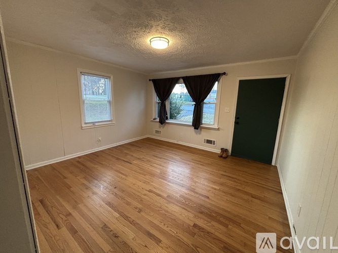 A room with wooden flooring and a window with curtains.