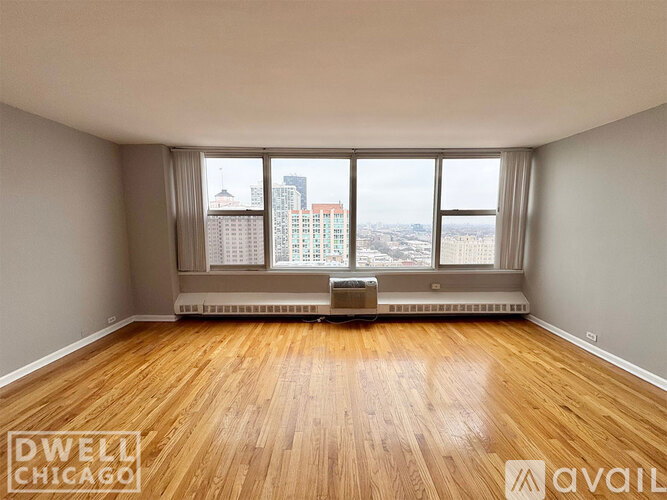 A room with wooden flooring and a large window overlooking a cityscape.
