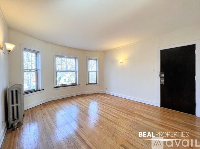 A room with wooden floors and white walls, with a black door on the right and a radiator on the left.