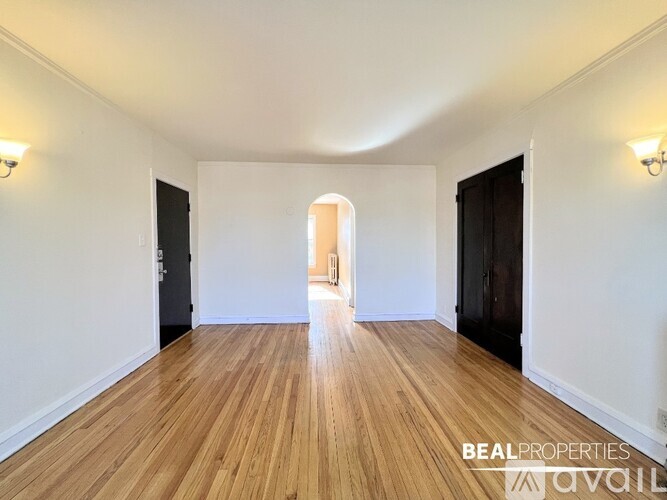 A spacious room with wooden flooring and white walls, with a doorway leading to another room.