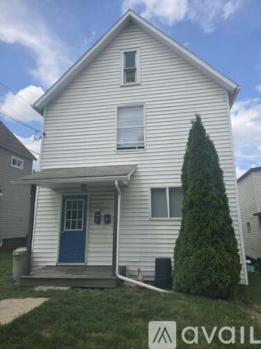 A white house with a blue door and a tree in front.