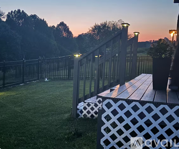 A wooden picnic table sits on a grassy area next to a metal fence.