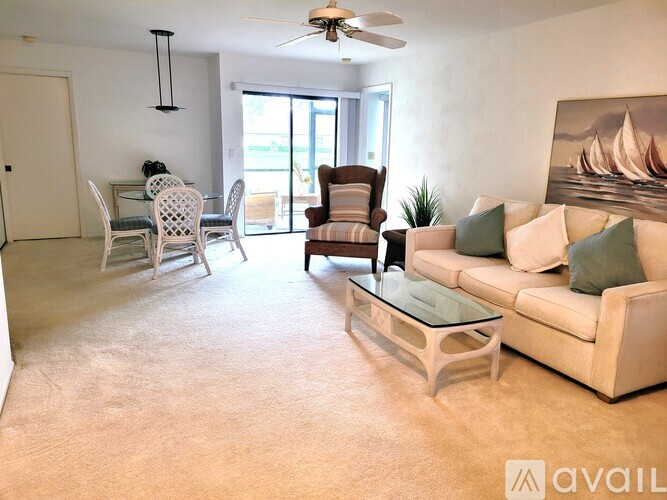 A living room with a white couch, a glass coffee table, and a painting of a sailboat on the wall.