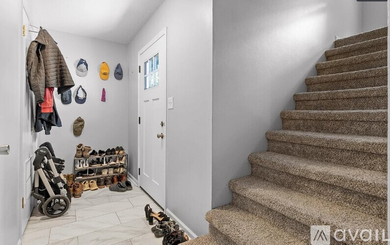 A hallway with a staircase and a coat rack with various items hanging on it.