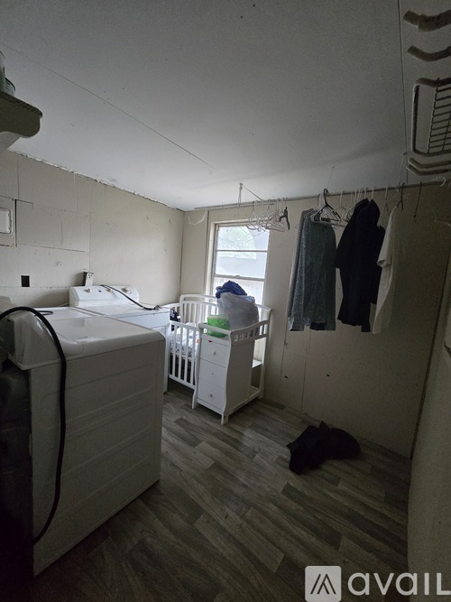 A baby crib sits in a corner of a room with a washing machine and clothes hanging on a rack.