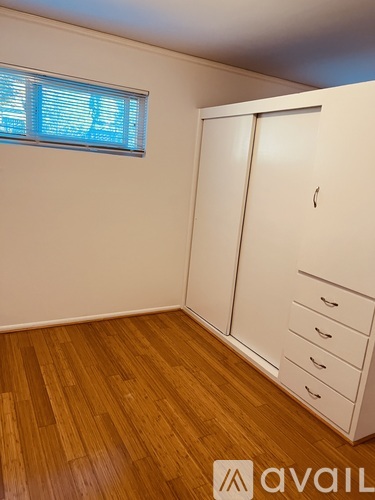 A room with a wooden floor and a white wardrobe with drawers.