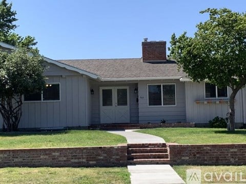 A house with a grey siding and a brick chimney is for sale.