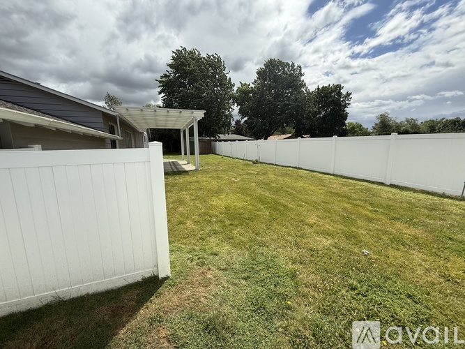 A white fence in a yard with a house and trees in the background.