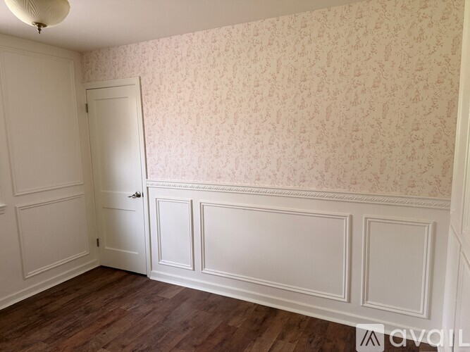 A room with a door, wallpaper, and wood flooring.