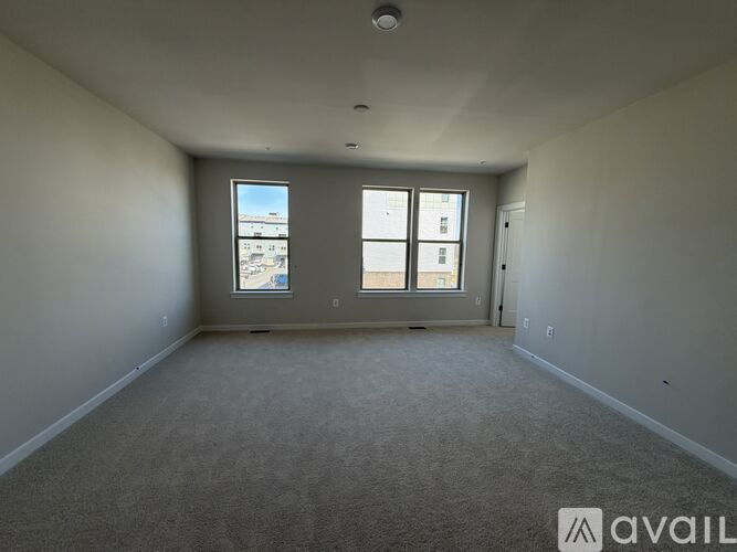 A spacious room with carpeted floor and two windows.