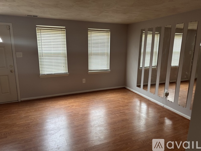 A room with wooden floors and two windows with blinds.