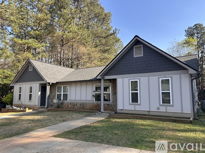 A house with a grey roof and white walls is surrounded by trees.