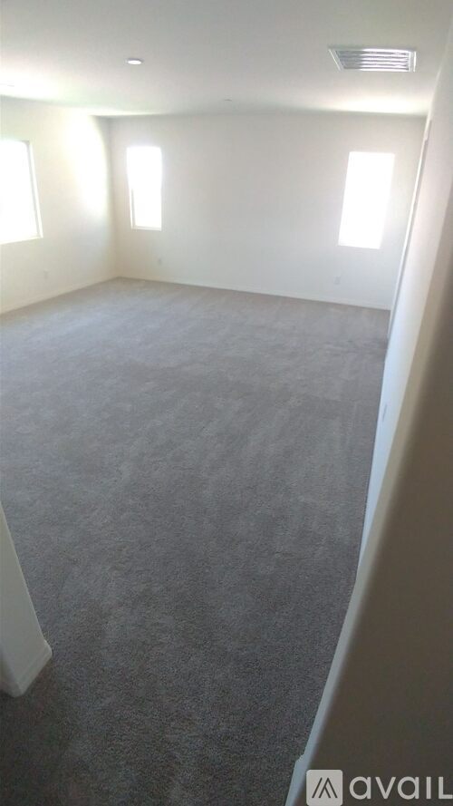 A room with grey carpet and three windows.