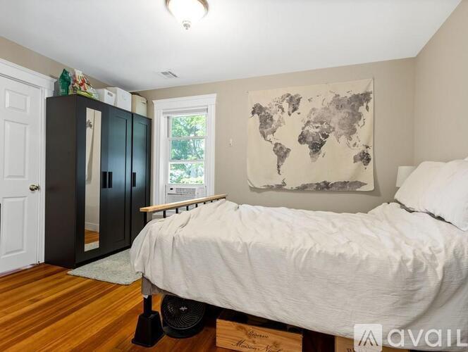 A bedroom with a bed, a world map on the wall, and a window with a view of trees.