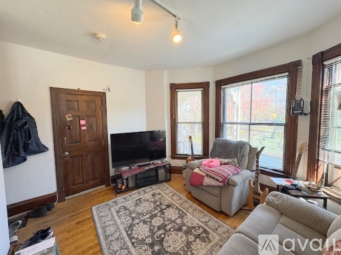 A living room with a grey couch, a grey chair, a grey rug, a wooden door, a television, and a window.