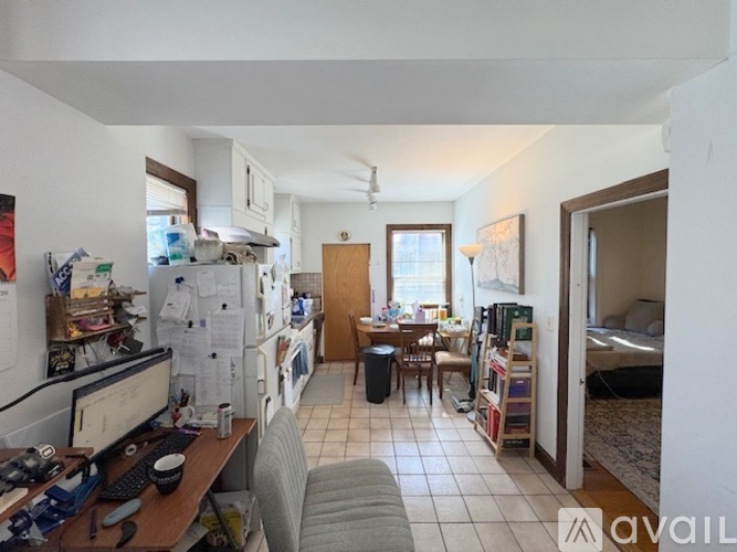 A kitchen area with a refrigerator, a desk with a computer, and a bedroom in the background.