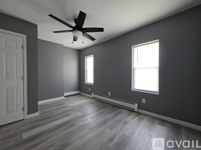 A spacious room with a ceiling fan and two windows.